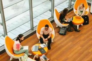 A bird’s eye view of several students sitting in orange and white lounge chairs in the Lowman Student Center; their laptops are out, and they are engaged in conversation.